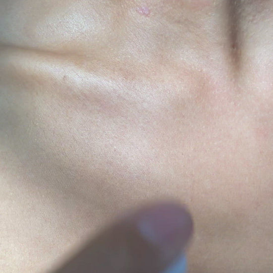 Slow motion and close up video of a hand applying Brown and Coconut Hydrating Face Oil to décolletage