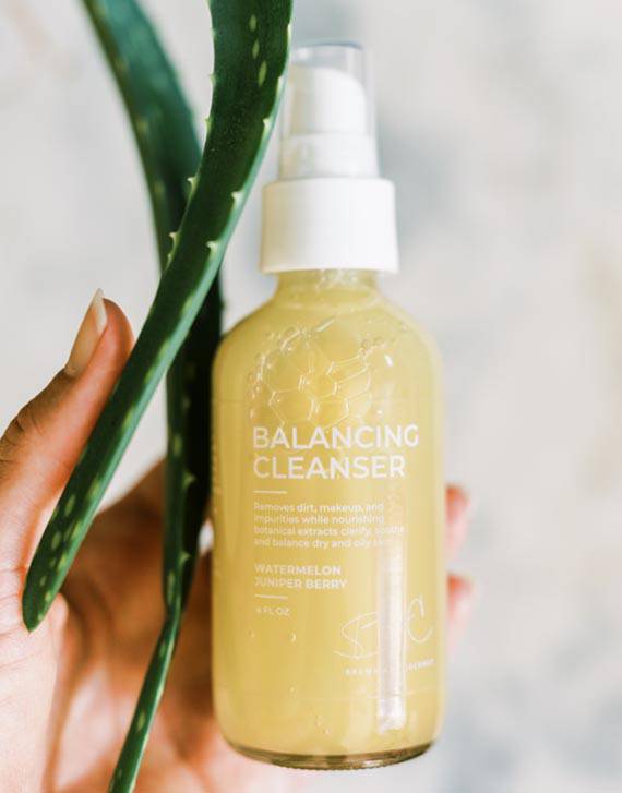 Hand holding two aloe vera leaves and one Brown and Coconut Balancing Cleanser