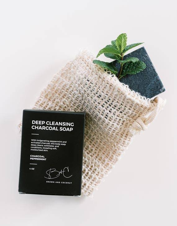 Brown and Coconut Exfoliating Soap Bag on white background with black soap box on top of bag and bar of soap and mint leaves sticking out of bag