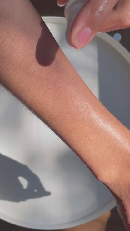 Slow motion video of a hand applying two pumps of Brown and Coconut Nouishing Body Oil onto an arm and rubbing into skin